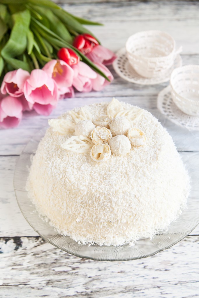 Coconut Cake for a valentine's day decorated with coconut candies. Delicate pink tulips on background