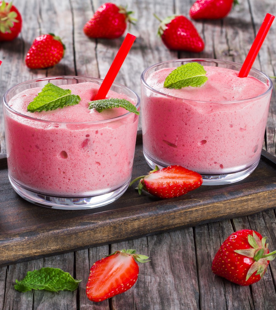 Strawberry Banana Smoothies Cups with straws and mint leaves on a dark brown wooden tray on an old rustic wooden table, studio lights, top view, close-up