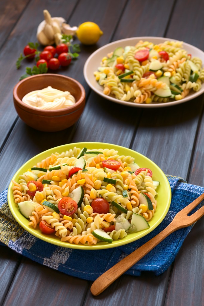 Two plates of vegetarian pasta salad made of tricolor fusilli, sweet corn, cucumber and cherry tomato with mayonnaise in the back, photographed with natural light (Selective Focus, Focus one third into the first salad)