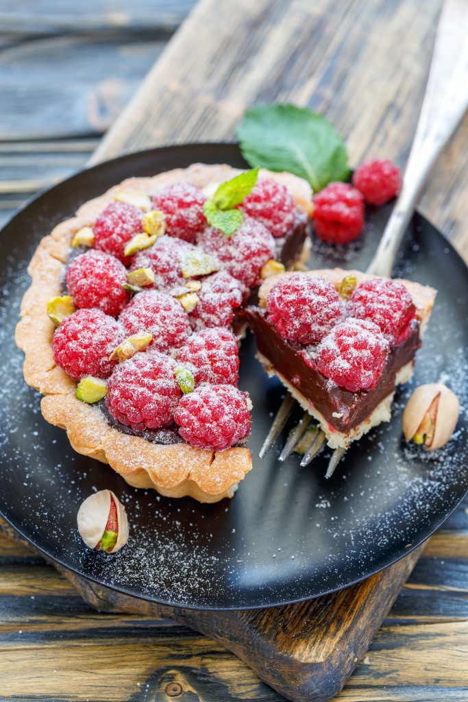 Plate of raspberry tart and fork on old wooden table, selective focus.