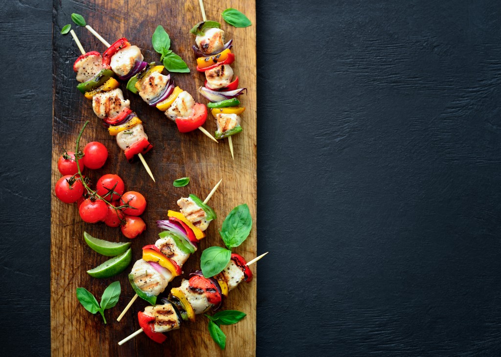 Chicken or turkey and vegetables cooked spicy skewers on a board, view from above, space for a text, dark culinary background
