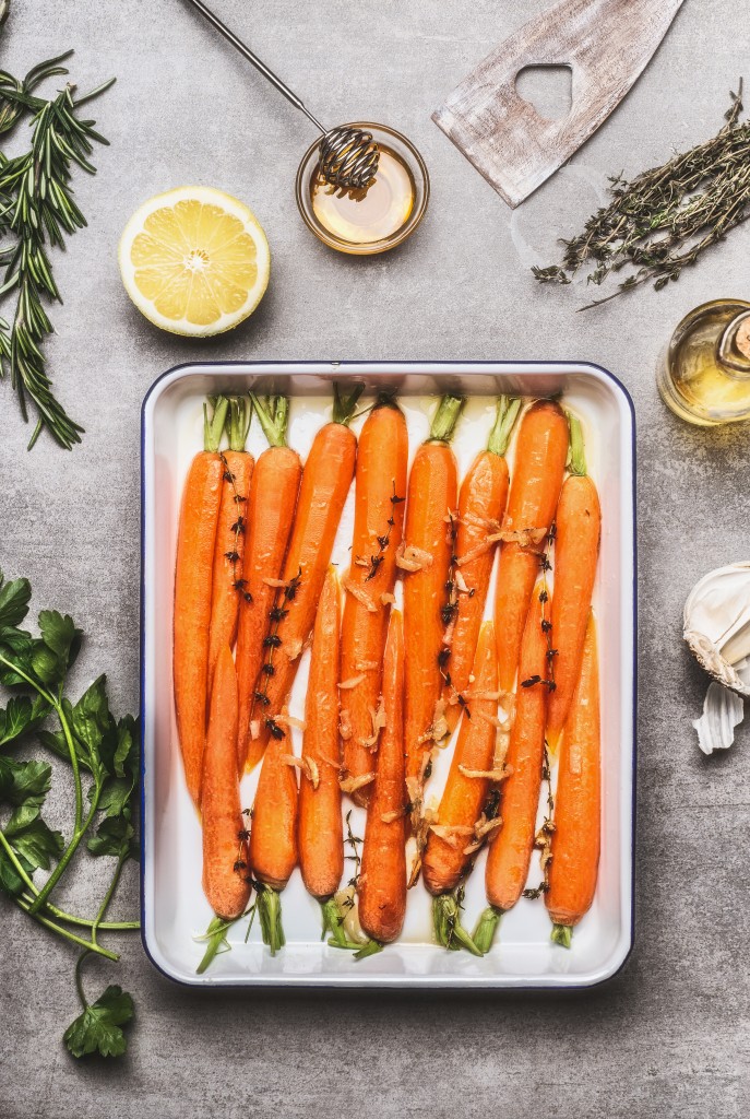Roasted Carrots with thyme, garlic, lemon and honey on baking try , cooking preparation. Healthy root vegetables concept