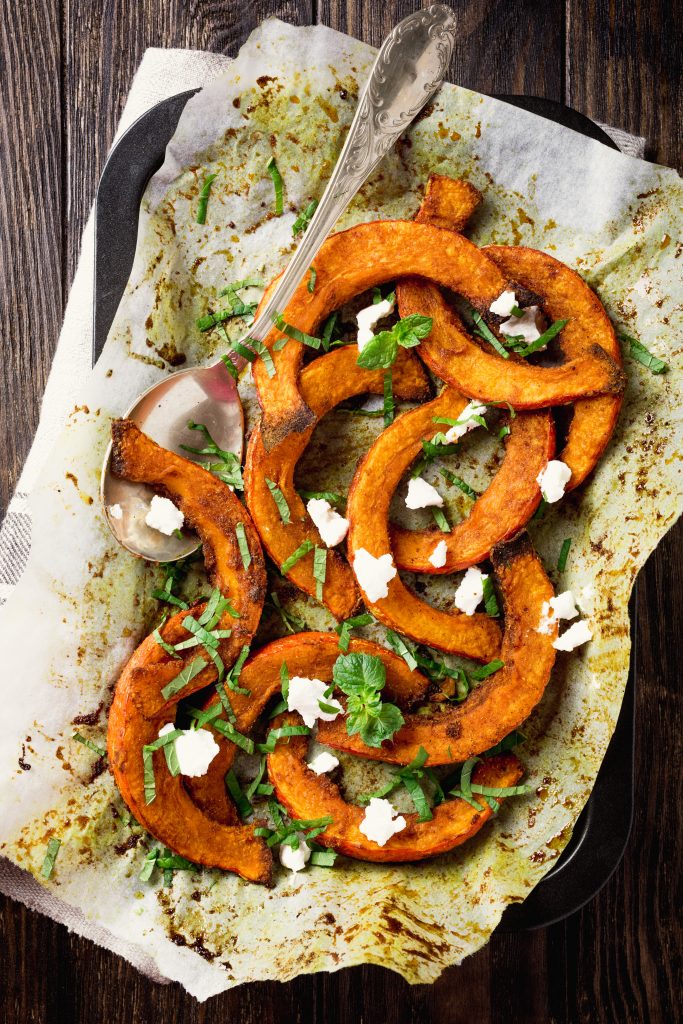 Roasted, baked pumpkin with addition aromatic herbs, goat cheese and mint. Healthy food concept with copy space. Top view.