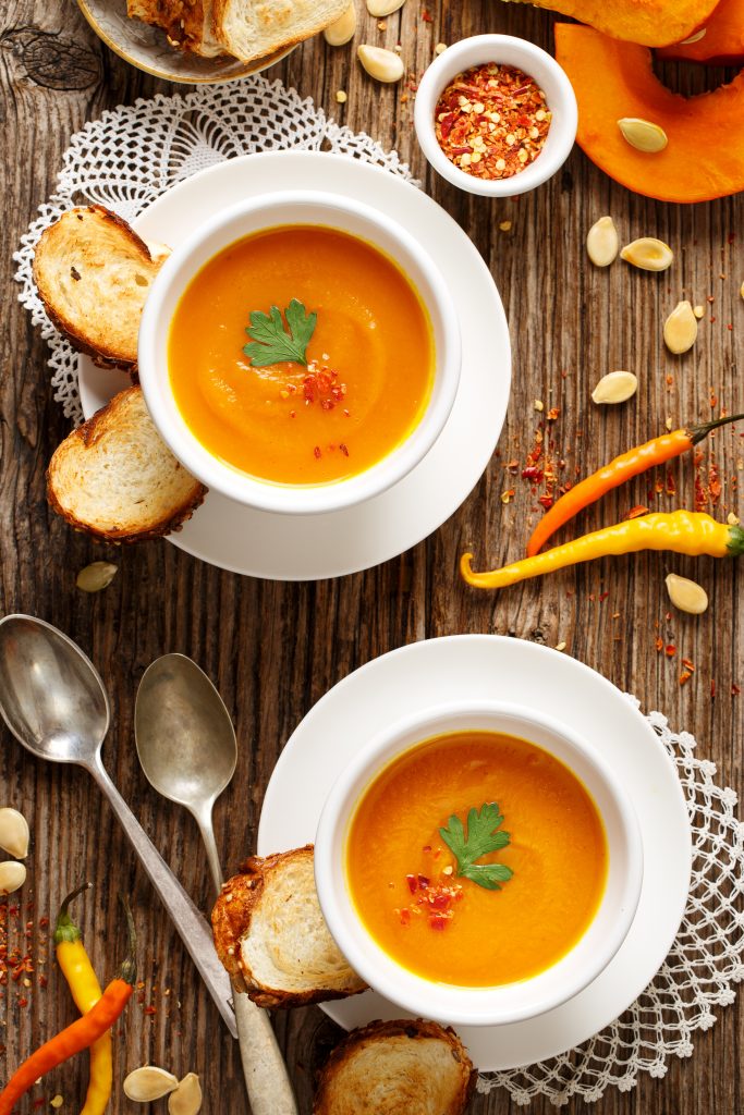 Homemade pumpkin soup in a white ceramic bowl on a wooden rustic table, nutritious and delicious vegetarian dish